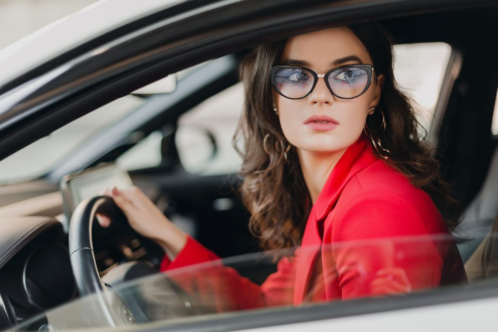 beautiful sexy rich business woman in red suit sitting in white car, wearing glasses